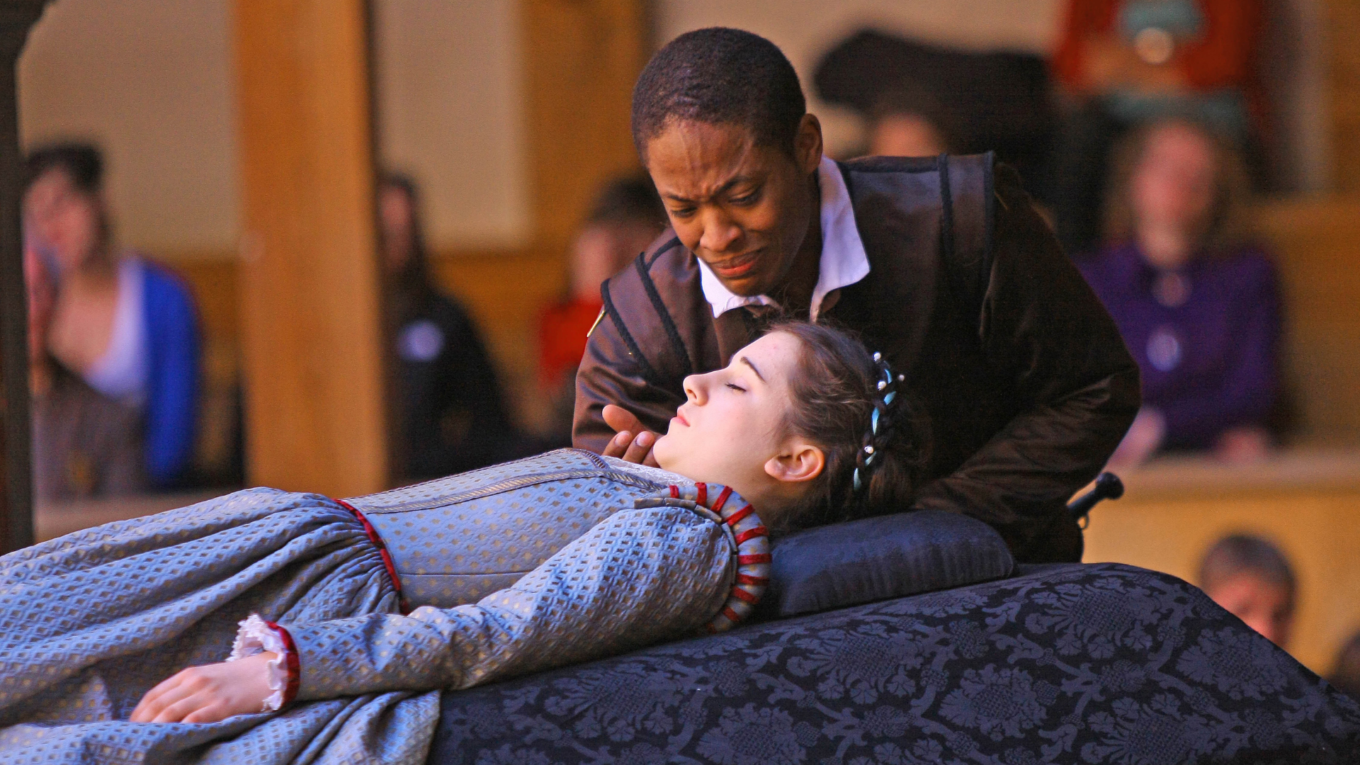 Actor Adetomiwa Edun (romeo), dressed in Elizabethan costume, leans over actor Ellie Kendrick (Juliet) who lays on a cushion presumably dead