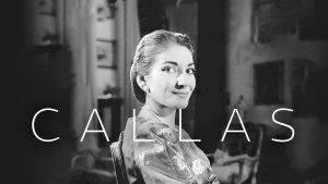 Maria Callas sits in a chair looking at the camera, the word Callas is set over the image. 