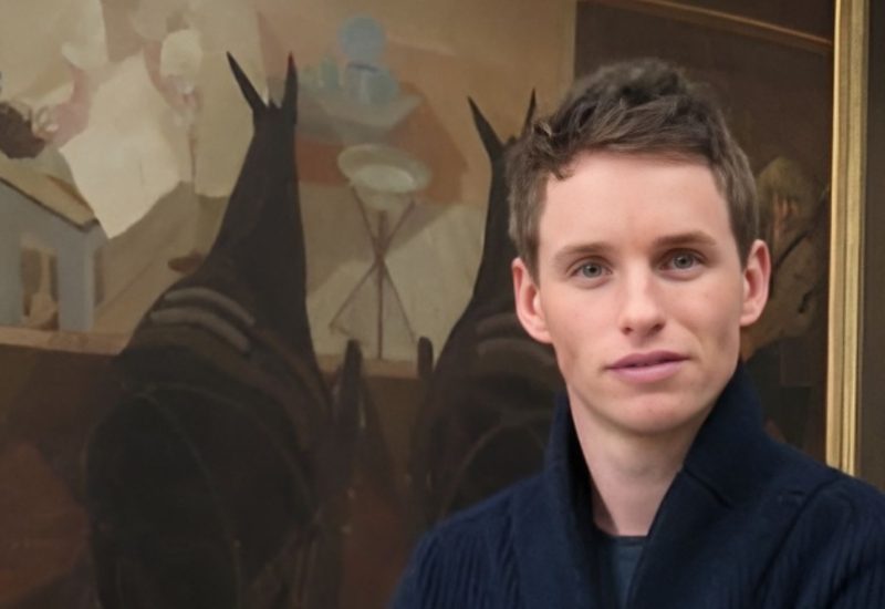 Eddie Redmayne stands in front of a painting depicting the horrors of WWI