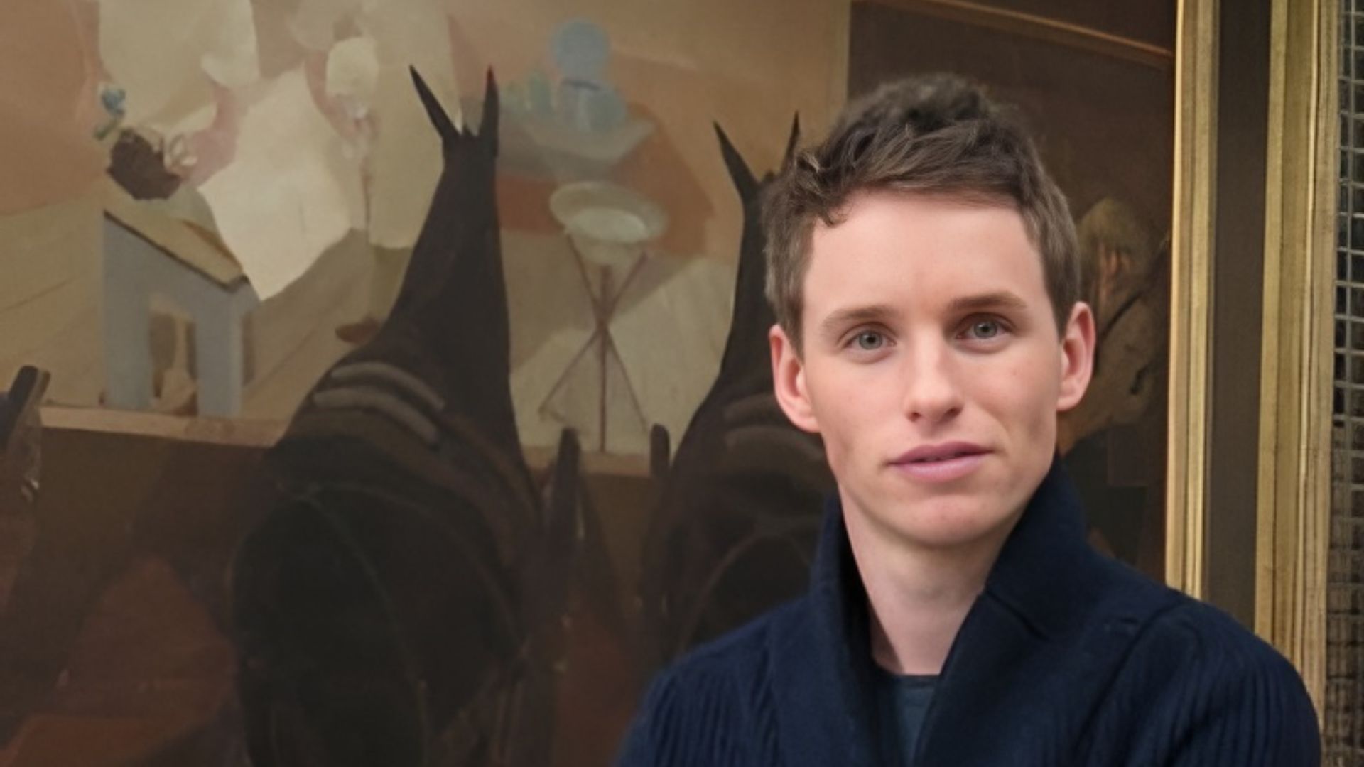 Eddie Redmayne stands in front of a painting depicting the horrors of WWI
