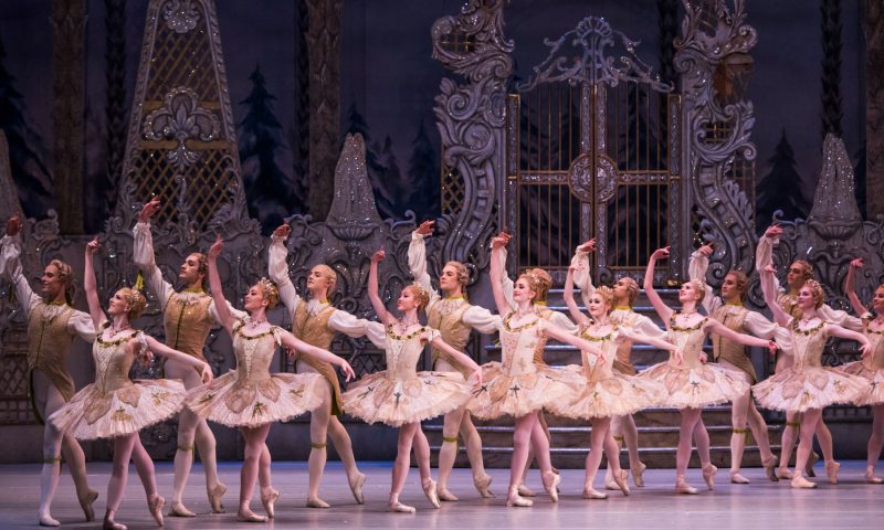 8 pairs of ballet dancers dressed in tutus and sparking 18th century inspired costumes stand on stage in a row in The Royal Opera House's production of The Nutcracker.