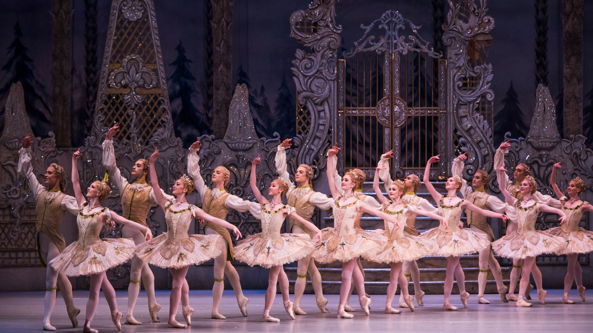 8 pairs of ballet dancers dressed in tutus and sparking 18th century inspired costumes stand on stage in a row in The Royal Opera House's production of The Nutcracker.